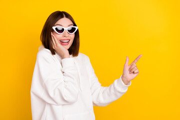 Wall Mural - Photo of excited promoter lady indicate finger empty space wear sunglass white hoodie isolated yellow color background