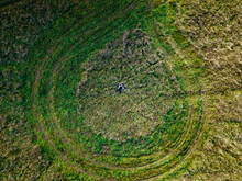 Aerial View Of Lone Woman Lying In Green Field Encircled By Tire Tracks