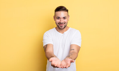 Wall Mural - young handsome man smiling happily with friendly, confident, positive look, offering and showing an object or concept