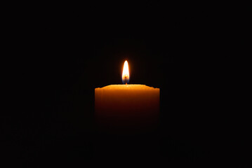 Wall Mural - One single light candle burning brightly in the black background.Spiritual candle yellow flame. Flame of candle in the darkness.Copy space.