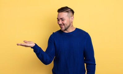 Wall Mural - young handsome man feeling happy and smiling casually, looking to an object or concept held on the hand on the side