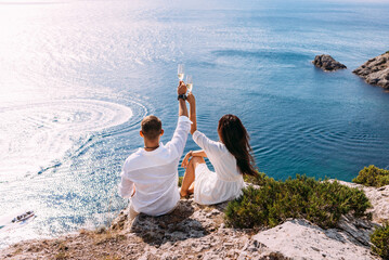 A couple in love on the shore drinking champagne, rear view. Vacation abroad. Holidays on the islands. A couple in light clothes is relaxing on the coast. Honeymoon. Wedding travel. Copy space