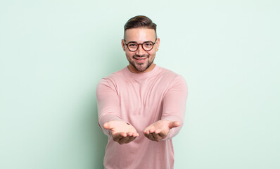 Wall Mural - young handsome man smiling happily with friendly, confident, positive look, offering and showing an object or concept