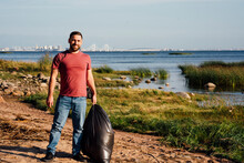Smiling Male Environmentalist With Garbage Bag At Riverbank
