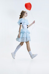 Wall Mural - Full-length portrait of young girl wearing Halloween dress, costume of clown walking isolated over grey background