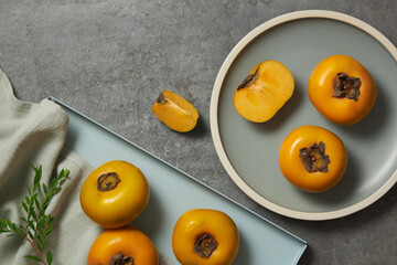 Wall Mural - Top view of persimmon in grey plate , flower , green leaf , light blue tray with grey background and blank space for advertising 