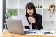 © kamiphotos - A beautiful Asian businesswoman sitting in her private office, she is checking company financial documents, she is a female executive of a startup company. Concept of financial management.
