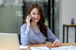© amnaj - Young Asian happy businesswoman communicating over mobile phone in the office.