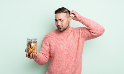 Wall Mural - young handsome man feeling puzzled and confused, scratching head. cookies bottle concept