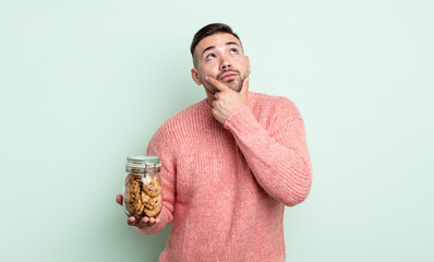 Wall Mural - young handsome man thinking, feeling doubtful and confused. cookies bottle concept