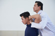 © DragonImages - Horizontal medium side view shot of modern mature Asian osteopathic therapist treating young man manipulating his bones and muscles