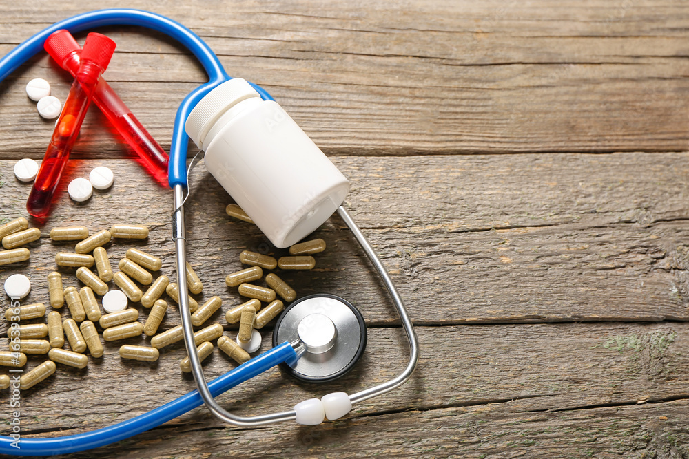 Composition with pills, stethoscope and test tubes on wooden background