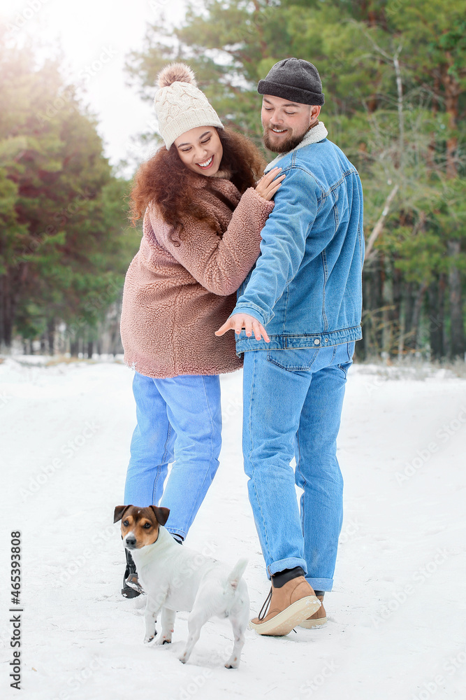 Happy young couple with dog in forest on winter day