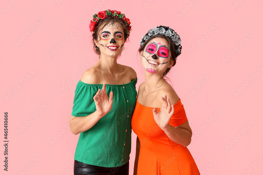 Stylish women with painted skull on faces against color background. Celebration of Mexico's Day of the Dead (El Dia de Muertos)