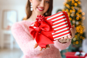 Beautiful young woman with Christmas gift at home