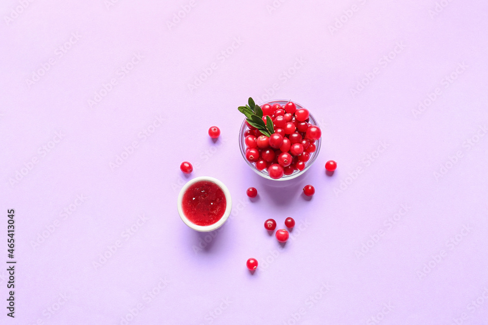 Bowls with lingonberry jam and berries on color background