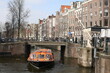 scenery of traditional brick houses and a orange long tour boat passing under the bridge of canal in winter amsterdam