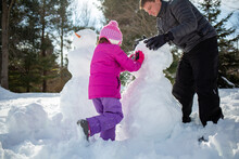 Father And Daughter Making A Snowman In Winter