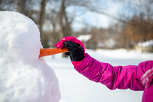 Young Girl Giving A Snowman A Carrot Nose On Cold Winter Day