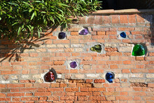 Vintage Brick Wall With Pieces Of Glass. Orange Brick Wall From Venice, Italy. Green Plant Overlook The Fence.