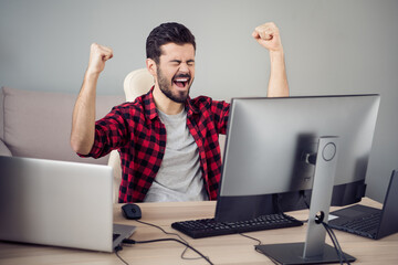 Photo of cheerful happy crazy young man celebrate win sit desk programmer job indoors in office inside workplace
