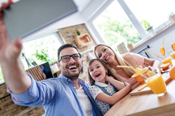 Wall Mural - Family making orange juice and taking selfie in the kitchen