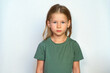 serious child looks at the camera. place for text. Portrait of a girl on a white background. Collected hair and green T-shirt. Cute smile happy smile. A cheerful preschool 