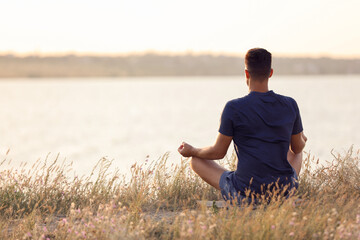 Man meditating near river on sunny day, back view. Space for text