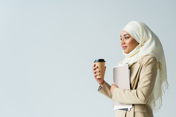 Wall Mural - Muslim businesswoman in hijab holding folders and paper cup isolated on gray