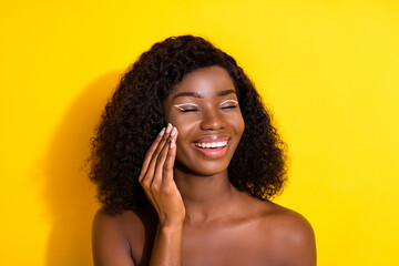 Wall Mural - Photo of young happy cheerful dreamy lovely afro girl applying cream on cheeks isolated on yellow color background