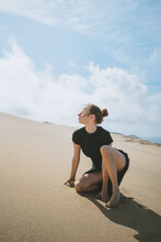 Woman Squatting On Sandy Dune In Arid Valley