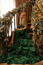 A Beautiful Blonde With Long Wavy Hair In A Chic Emerald Long Evening Dress Is Sitting On The Steps Of A Staircase Decorated With Christmas Toys