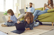 © Studio Romantic - Modern family using digital devices. Little child lying on floor at home searching for games on tablet while mum is using smartphone and brother and dad are using laptops. People, technology concept