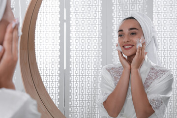 Sticker - Beautiful young woman applying cleansing foam onto face near mirror in bathroom. Skin care cosmetic