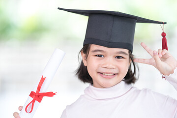 Portrait happy Asian female school kid graduate in a graduation cap holds a rolled certificate paper. Graduation Celebration Concept Stock Photo