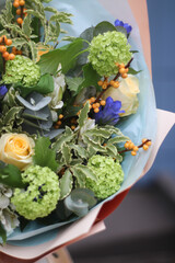 part of a bouquet of bright orange ilex berries and yellow roses, with green viburnum flowers and other blue flowers