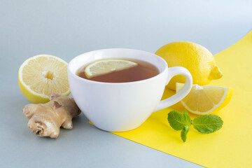 Wall Mural - Tea with lemon and ginger in the white cup on the gray  yellow background. Close-up.