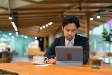 Wall Mural - Portrait of Asian businessman in coffee shop using digital tablet computer