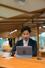 Wall Mural - Portrait of shocked Asian businessman in coffee shop using digital tablet computer