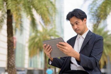 Wall Mural - Asian businessman sitting outdoors in city using digital tablet computer