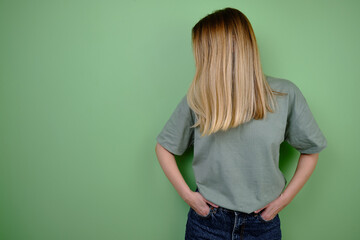 Wall Mural - Girl model posing near a green wall in a green t-shirt and jeans. Hand gestures and emotions. Studio shot of a girl. Emotion and beauty concept. Casual wear