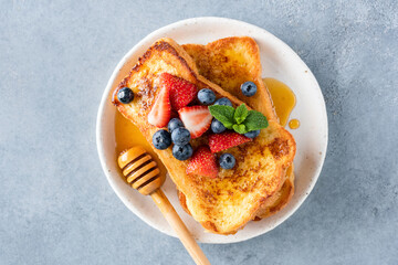 French toasts with honey and fresh berries on white plate, table top view. Sweet breakfast or dessert food