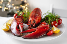 Crop Shot Of Freshly Cooked Red Lobster With Vegetables On A Plate And White Table. Christmas Light On A Background. Holidays Food Concept
