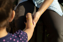 A Woman Holds The Girl's Hand, Close-up. Mother In Denim Shirt And Black Pants, Daughter In Purple Polka Dot Dress. On The Hands Of The Child Drawing With Yellow Paint. Drawing On The Body