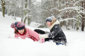 Wall Mural - Two young girls having fun together in beautiful winter park. Cute sisters playing in a snow. Winter activities for family with kids.