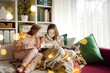 © MNStudio - Two young sisters snuggling up on the sofa in a cozy living room at Christmas. Cute children using a tablet at home during winter break. Kids reading a book in comfy blanket.