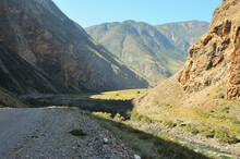 A Crushed Stone Road Running Along The Bottom Of A Deep Canyon In The Mountains Along The Bank Of A Beautiful River.