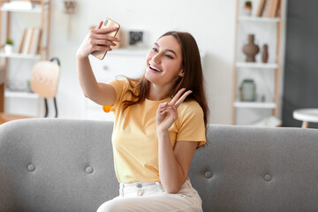 Canvas Print - Beautiful happy woman sitting on sofa and taking selfie