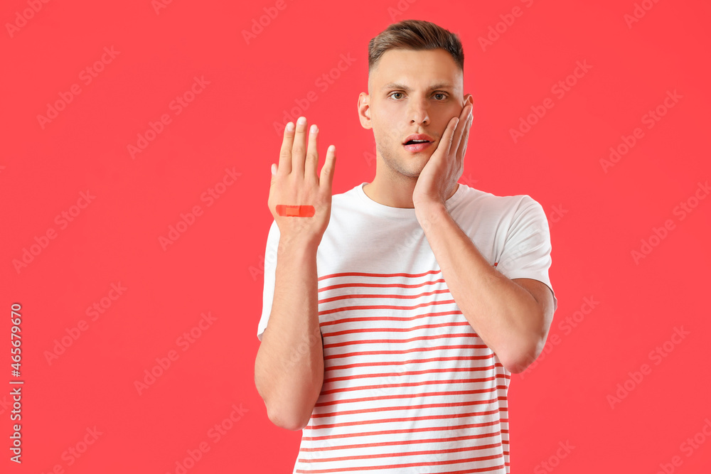 Shocked man with medical patch on his hand against color background