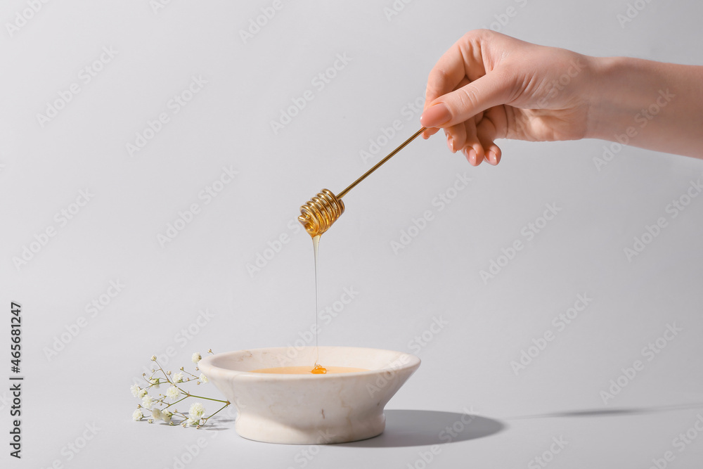 Woman pouring honey from dipper into bowl on grey background